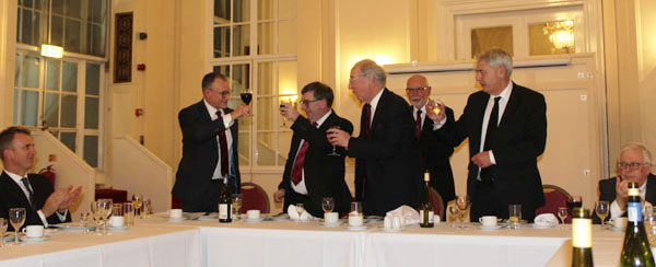 Ian Sanderson (standing left) toasts the three principals, looked on by John James