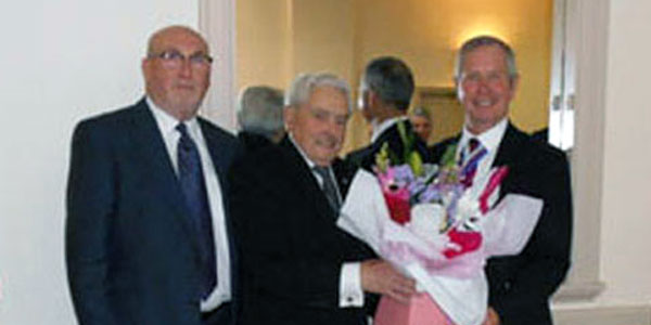 Barry Elman (centre) presenting a bouquet of flowers to Steven (right).