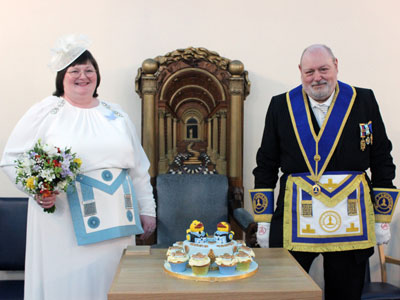 Mark and Tanya in their regalia after the wedding with their wedding cake on the master’s pedestal with the magnificent master’s chair.