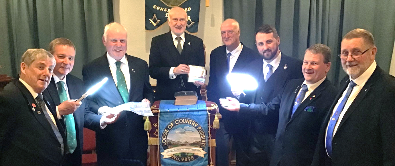 Using lighted magnifiers to examine the gold sovereigns and Masonic tokens. Pictured from left to right, are: Peter Roberts, Colin Preston, Ian Heyes (WM of Country Pursuits Lodge of West Lancashire), Bob Reeves, David Holgate, David Jenkinson, Richard Dennison, Bob Malcolm.